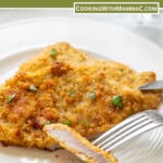 a fork piercing a piece of breaded, fried veal cutlet on a white plate