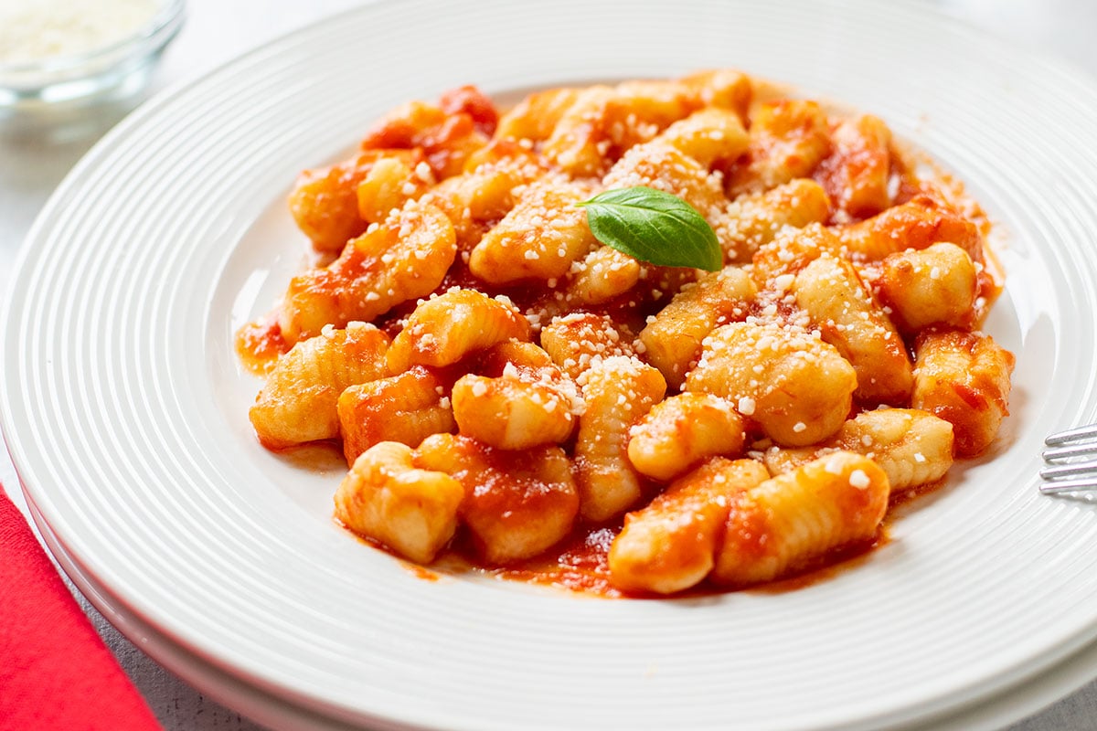 plate of homemade gnocchi topped with tomato sauce and basil